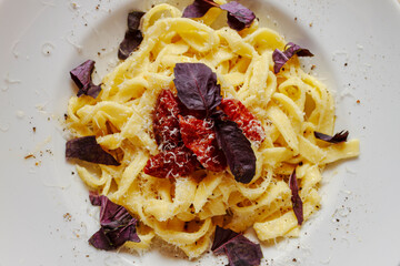 Top view of cooked pasta with sun dried tomatoes, purple basil and parmesan cheese on white plate.