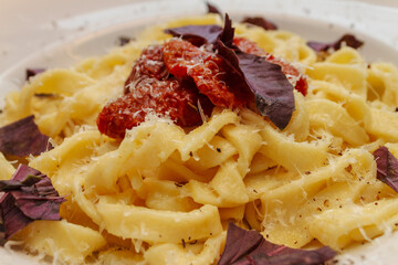 Close up of creamy pasta dish with sun dried tomatoes and fresh purple basil leaves. Appetizing italian food.