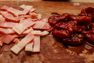 Close up of sliced ham and sun dried tomatoes on wooden surface. Ingredients for carbonara or pasta sauce.