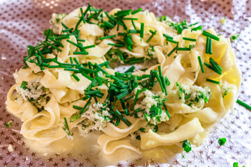 Creamy pasta noodles topped with fresh chopped green chives or onions on foil. Simple homemade meal.