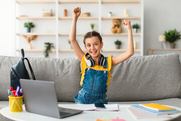 Academic Achievement Concept. Portrait Of Excited Pupil Girl Sitting In Living Room With Laptop Gesturing Yes Shaking Clenched Fists Getting A-Grade During Webinar At Home. Online School Tests Concept