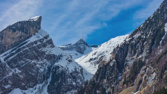 Time lapse, view on snowy mountain peak above the forest. Saentis mountain peak in the Appenzell Alps. Switzerland