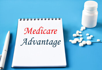 MEDICARE ADVANTAGE - words in white notebook on blue background with pills and pen