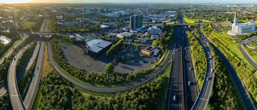 Aerial view of Manukau, Auckland, New Zealand, showing the city skyline, highway traffic, commercial buildings, and the Auckland New Zealand Temple. Illustrates urban planning and transportation.