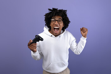 Triumphant black teen guy with joystick shouting in excitement, playing video game, making YES...
