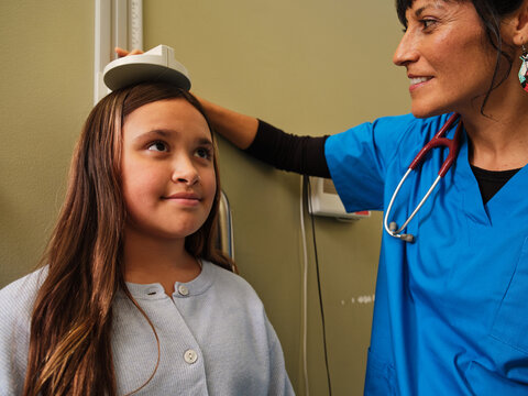 Native American nurse in scrubs checking child's growth