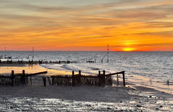 A rich orange sunset over Hunstanton beach with old wooden groynes in the foreground, Norfolk, England, UK. 