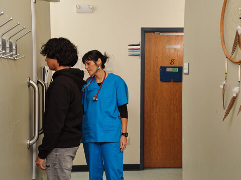 Indigenous nurse in scrubs measures teen boy's weight