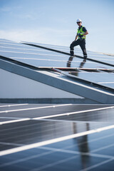 Obraz premium Technician installing solar panels on factory roof for green energy. A skilled technician in safety gear is working on a solar panel installation on rooftop.