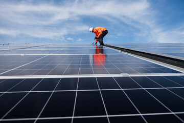 Technician installing solar panels on factory roof for green energy. A skilled technician in safety...