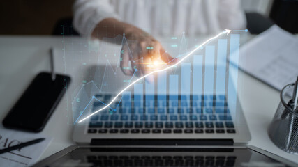 A business professional uses a laptop to analyze growth data, featuring a futuristic digital graph overlay that symbolizes financial performance trends in a modern office environment. Impute