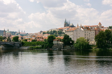 Fototapeta premium View of Prague with buildings, water, and clouds on a sunny day near the river