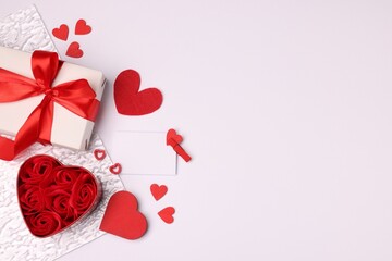 Beautiful roses, romantic gift and decorative hearts on white background, flat lay. Space for text