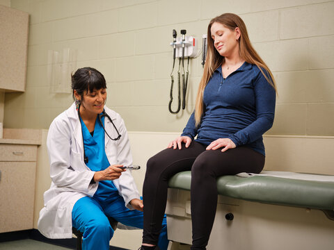 NP in blue scrubs tests woman's knee reflexes