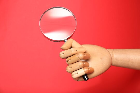 Mannequin hand with magnifying glass on red background, closeup
