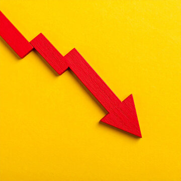Red wooden arrow pointing downward, yellow backdrop. Economic downturn, business, market decline