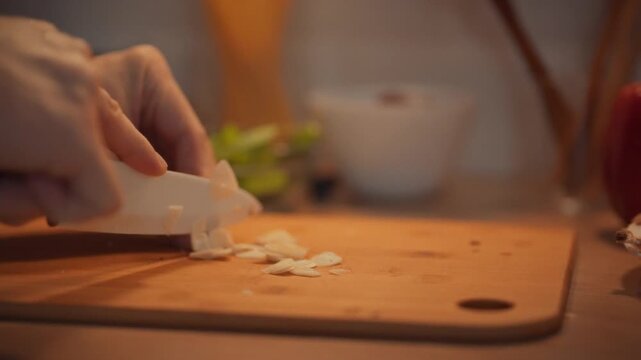 A cook chops a nutritious vegetable, garlic cloves, into fine pieces using a sharp knife, releasing its aromatic spice and potent antiseptic enzymes, adding health benefits and vitamins to the dinner