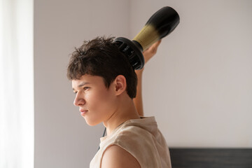 Fashion teenage boy blow-dries his hair, hair styling, personal care concept