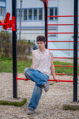 Teenager leaning on red metal bars at an outdoor fitness area, wearing wireless earbuds
