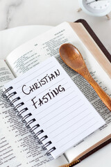 Christian fasting, handwritten text in notebook with wooden spoon, holy bible, and alarm clock. Top view. Spiritual food, patience, scripture study and repentance, biblical concept.