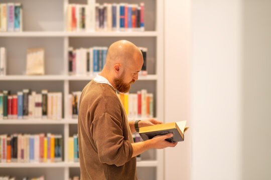 Smart man choosing book from bookshelf. Textbook resources in library for educational research and reading