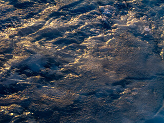 Abstract close-up of frozen water with textured ice surface and golden light reflections, creating a cold winter background with natural patterns, blue tones and copy space