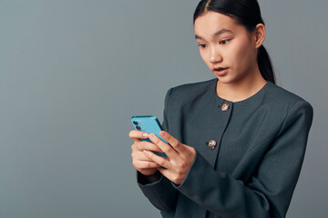Woman holding smartphone with both hands looking surprised or shocked with mouth slightly open...