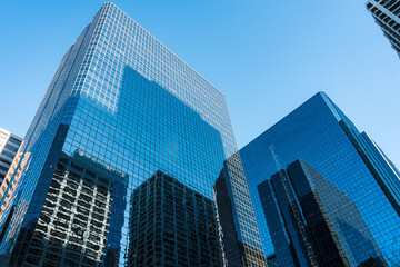 Fototapeta premium View of city skyscrapers with glass facades mirroring the sky, symbolizing architectural innovation and urban growth in the modern landscape. Skyscrapers are reaching high into the blue sky.