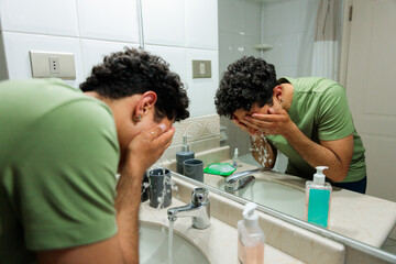 Obraz premium Young Latin man washing his face at a bathroom sink, showing personal hygiene, self care, and morning preparation