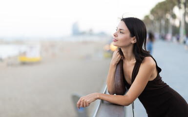Fototapeta premium Elegant young woman in summer dress leaning on parapet at Barceloneta beach promenade