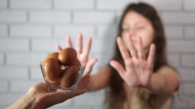 Girl rejecting eggs due to food allergy. Young girl with a food allergy showing a stop gesture with her hands, refusing to eat the chicken eggs offered to her, representing the concept of intolerance