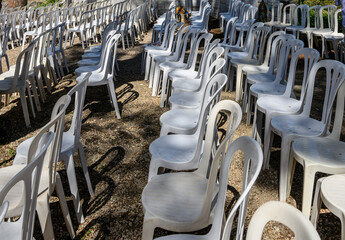De nombreuses chaises en plastique blanc sont dispos&eacute;es &agrave; l'ext&eacute;rieur sur une surface en gravier, projetant des ombres au soleil