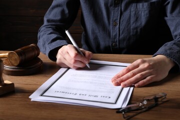 Woman signing Last Will and Testament at wooden table, closeup