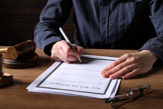 Woman signing Last Will and Testament at wooden table, closeup