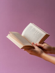 Fototapeta premium Hands holding an open paperback book with text on faded mauve background suitable for education themed or literary stock photography purposes
