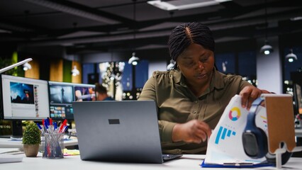 Black company worker checking market research and graphs on a laptop, examining insights and reports for data visualization in the workspace. Resource allocation strategy for goals. Camera A.