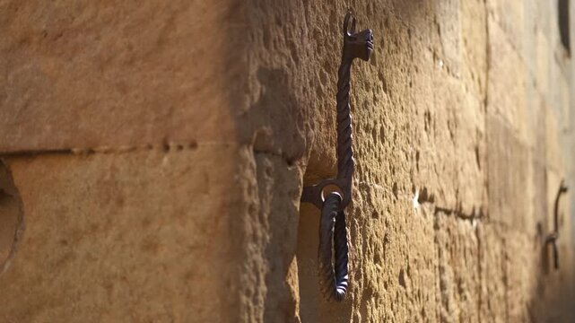 Wrought iron horse tether rings on the wall of an old stone building. Antique wrought iron horse tether rings with decorative details are attached to the weathered stone wall of a historic medieval