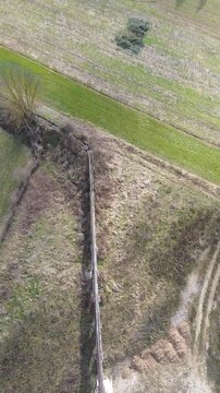 Cinematic vertical drone footage of Tanaro River with ancient Roman bridge and Bagnasco city on the left bank and old mill on the right bank captured on a sunny winter day