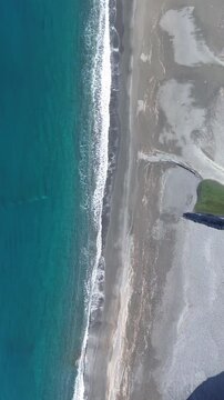 Vertical drone footage of a sandy coastline with winter waves crashing on the beaches enhancing the contrast between the blue sea and white wave lines