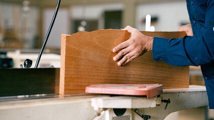Craftsman hands guiding a wooden plank through a woodworking machine, shaping the timber for a new project