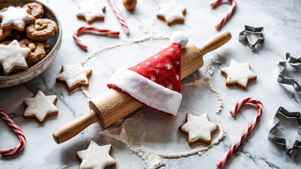 Rolling pin with Santa hat surrounded by holiday cookies and candy canes