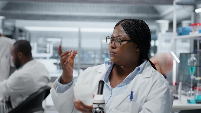 Female molecular biologist studying genetic tissue sample on glass slide under magnification. African american woman searching for mutation patterns using advanced optical equipment, camera B