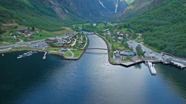 Aerial view of Gudvangen harbour and village by the fjord in Norway. Drone footage shows docks, boats, river mouth and green valley surrounded by steep mountains.