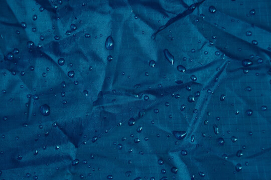 Close-up of water droplets on blue waterproof ripstop fabric texture. Concept of water resistance and outdoor gear.