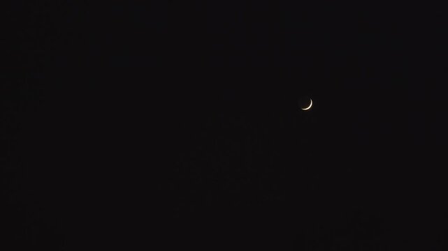 A thin crescent moon shines in a static night scene. The sky is pure black, free of stars or clouds, emphasizing the quiet elegance and clarity of the lunar phase in deep darkness.