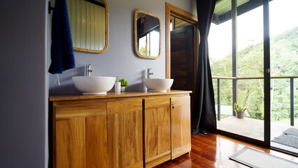 Modern bathroom featuring a wooden double vanity, two round sinks, and large glass doors overlooking a tropical forest