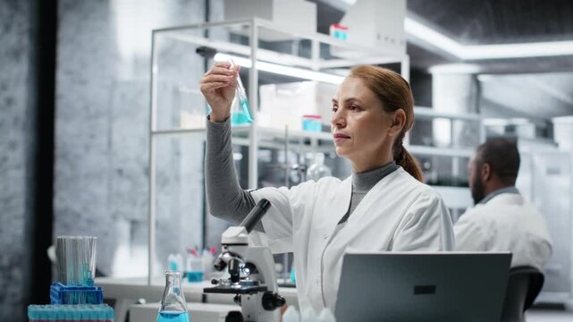 Scientist in lab pipetting blue liquid into test tube to analyze it. Laboratory worker transferring chemical sample to prepare for immediate spectroscopic analysis, camera B