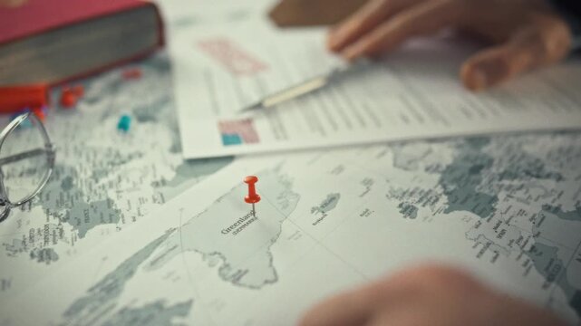 A large world map on the table features a red pin marking Greenland's territory, highlighting the island's autonomy and sovereignty within the Kingdom of Denmark, surrounded by the vast Atlantic Ocean