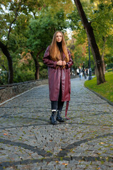Woman in long maroon coat standing on cobblestone path in park