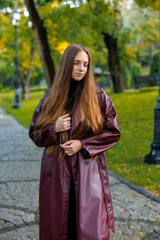 Young woman in burgundy coat poses outdoors in park with trees